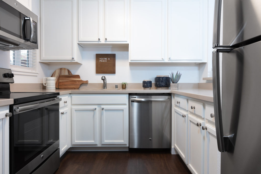 Dog-Friendly Apartments In Sunnyvale, CA - The Grove Garden - A Kitchen With White Cabinetry, Stainless Steel Appliances, And Dark Wood Flooring.
