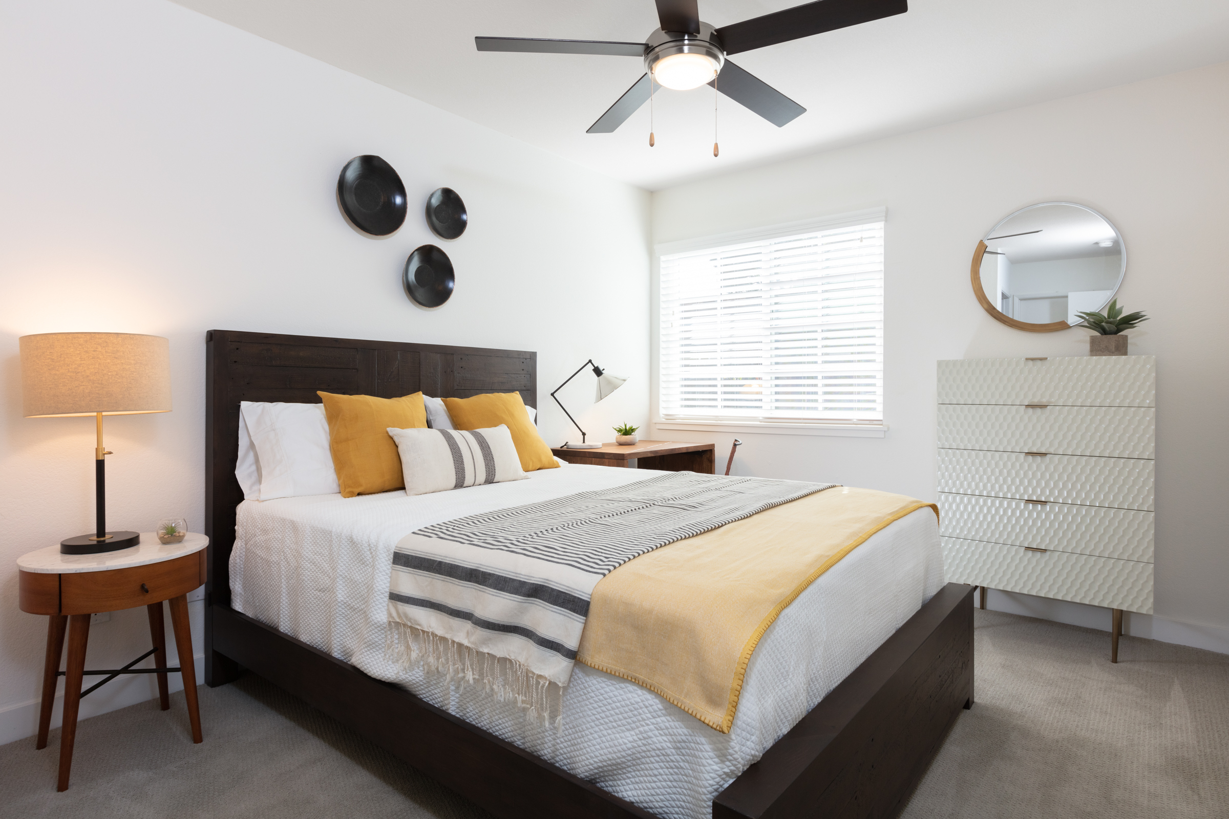 Pet-Friendly Apartments In Sunnyvale, CA - The Grove Garden - A Modern Bedroom With Dark Wooden Headboard, Ceiling Fan, And A Round Side Table With A Lamp.