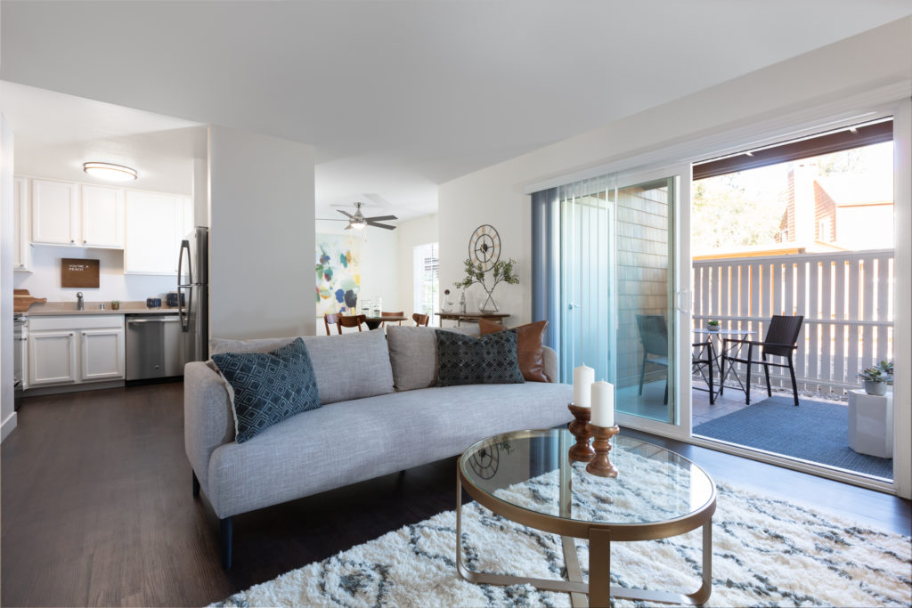 Apartments Near San Jose - The Grove Garden - An Open-Concept Living Area With A Sofa, A Privacy Fence, Sliding Glass Doors, Outdoor Chairs, And A Small Table.