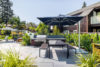 Gas grill with picnic table in the foreground surrounded by lush landscaping.