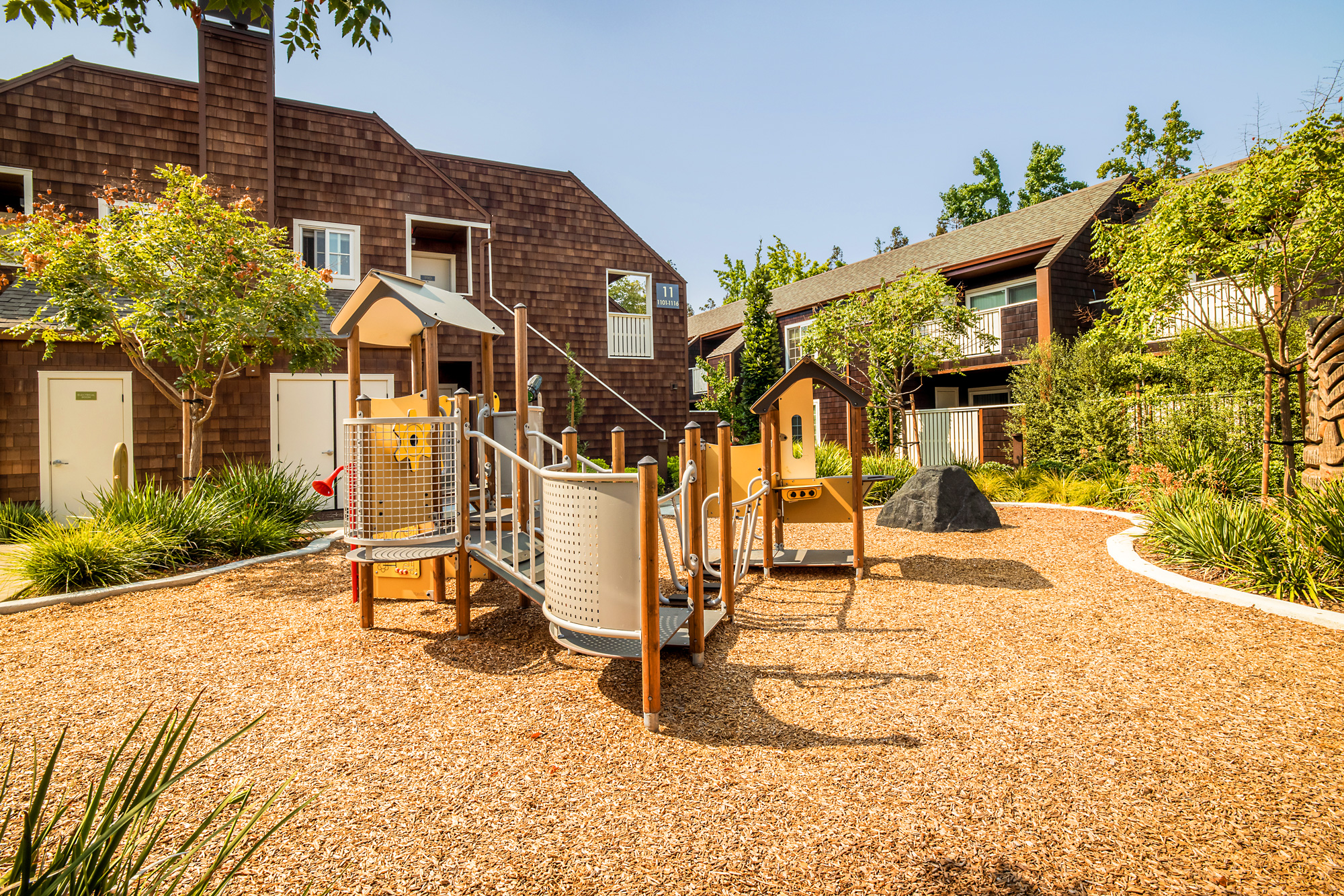 Playground surrounded by green landscaping and apartments.