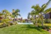 Palm trees, neatly cut grass next to outdoor pool with showers.